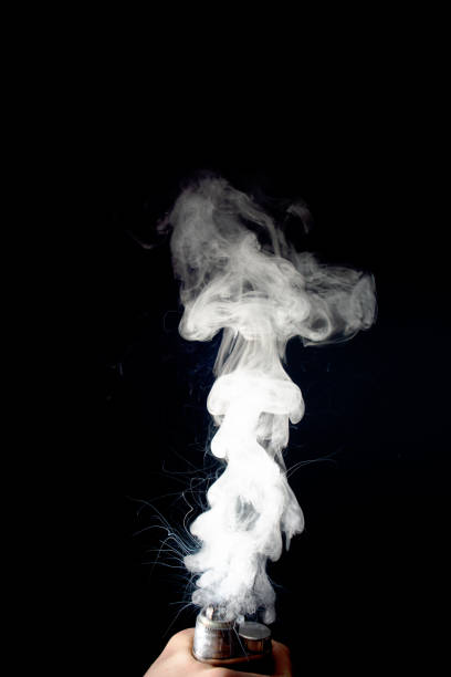 istock Male hand holds vape without atomiser. Column of vape clouds splash from coil on black background. Fog is white. Stock isolated white smoke with spray boiling glycerine. 1133084076