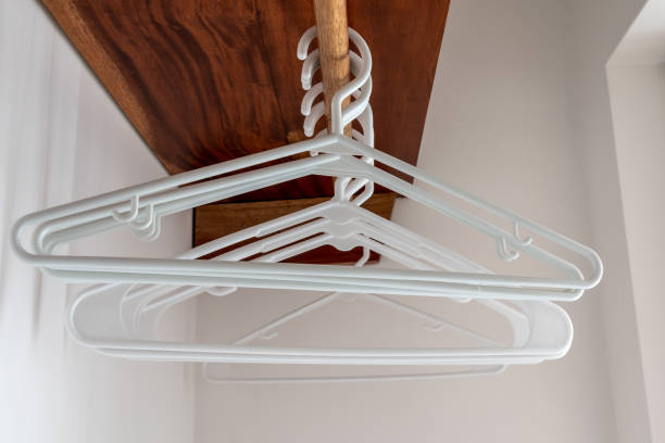 Empty white plastic hangers in closet Empty white plastic adult clothes/coat hangers hanging in bedroom closet on wooden rod below wooden shelf. clothes hanger rod stock pictures, royalty-free photos & images