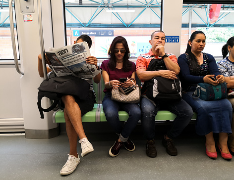 Medellin, Antioquia, Colombia - 11/24/2018: Passengers sitting inside a train (metro). Person reading the newspaper while traveling on public transport. A woman using her cell phone.