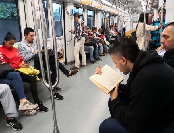Interior of train car of the Medellin Metro. Adult man reading a book on the go Interior of a train car of the Metro of Medellin (Colombia). In the foreground, an adult man reading a book on the go. People, passengers, on the train, sitting, using their cell phones or waiting to reach their destination. metro medellin stock pictures, royalty-free photos & images