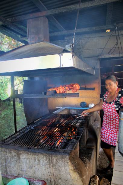 Pork Cooking Over an Open Fire Limon, Costa Rica 29 January 2019:  A local StreetSide vendor cooks and servs her pork to locals who pass by on their way home from work. puerto limon stock pictures, royalty-free photos & images