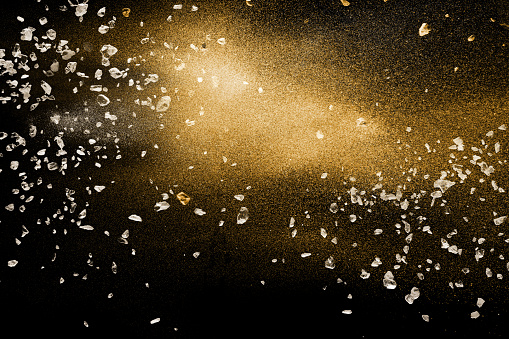 Split debris of stone exploding with golden dry river sand against black background.