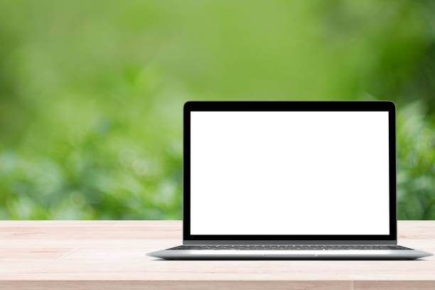 Empty wooden table with blank screen laptop on green blurred abstract background from foliage background. Ready used us display or montage products design stock photo