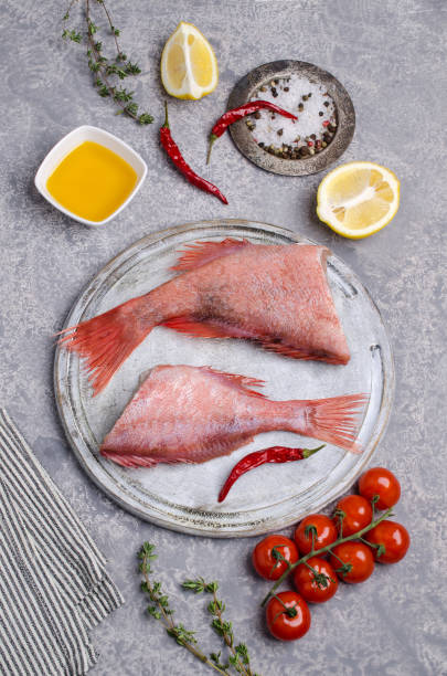 Fish raw snapper Fish raw snapper with lemon slices, tomatoes and spices on a slate background. Selective focus. sebastinae photos stock pictures, royalty-free photos & images