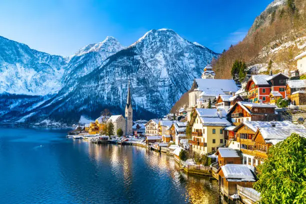 Photo of Classic postcard view of famous Hallstatt lakeside town in the Alps with traditional passenger ship on a beautiful cold sunny day with blue sky and clouds in winter, Salzkammergut region, Austria