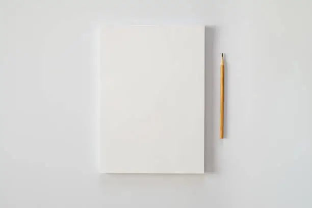Photo of A stack of blank sheets of paper and a pencil on a white background. Creative crisis or the beginning of a new novel.