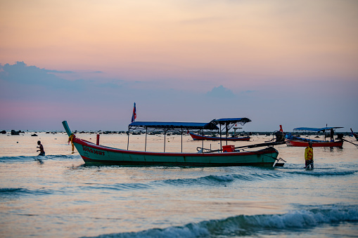 Pakarang beach (Takua Pa) at sunset. There are long tail boats silhouetted against the night sky and their owners are wading out to reposition them for high tide.