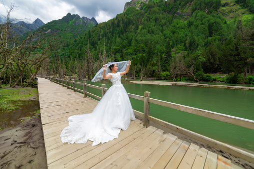 The woman in the wedding dress is by the lake in the forest.