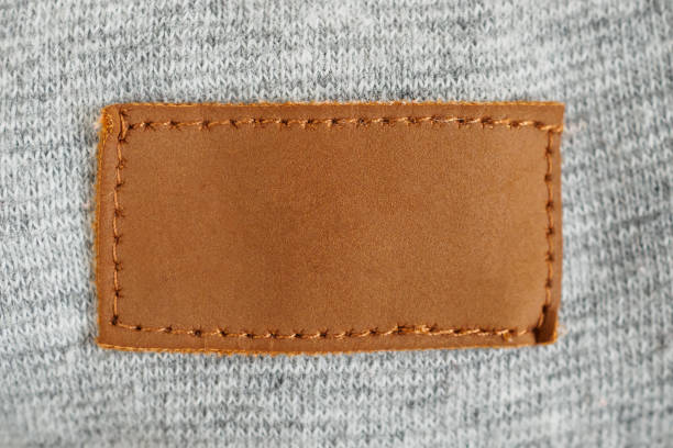 灰色の織物の織物の背景のブランク茶色の革布のラベル - leather sewing label patch ストックフォトと画像