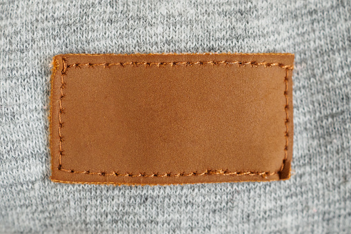 Blank brown leather cloth label on gray fabric textile background
