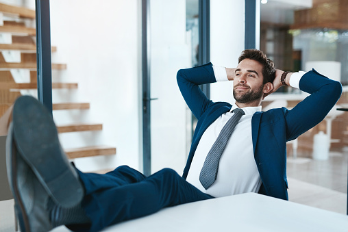 Cropped shot of a handsome young businessman relaxing with his feet up on a desk in a modern office
