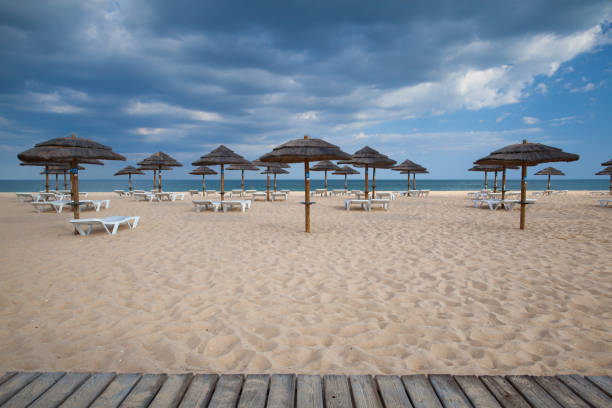 Straw sunshade on a pristine deserted sandy beach, with clear blue sky, on the Caparica Coast near Lisbon, Portugal.