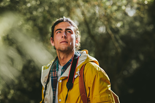 Close up of a man wearing jacket and backpack on an exploration trail. Side view portrait of a traveler standing outdoors looking away.