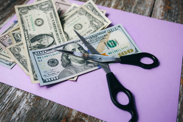 istock Dollar banknotes with scissors lying on the purple pastel background. Money notes on the surface. Devaluation of a currency. Business and society problems. 1133154405