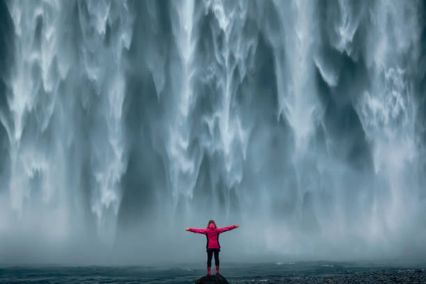 Famous powerful Skogafoss waterfall at south Iceland Iceland landscape photo of brave girl who proudly standing with his arms raised in front of water wall of mighty waterfall. adventure stock pictures, royalty-free photos & images