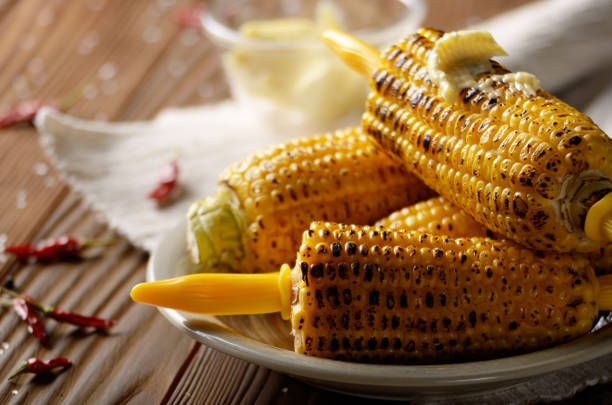 istock Wooden table with deep grilled sweet corn cobs under melting butter with plastic holder on clay dish 1133158941