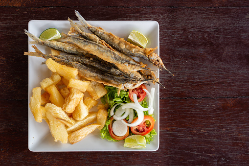 Agulha frita (typical fried fish from Pernambuco beaches, Brazil northeast) ready to eat with salad and fried cassava. Overhead view