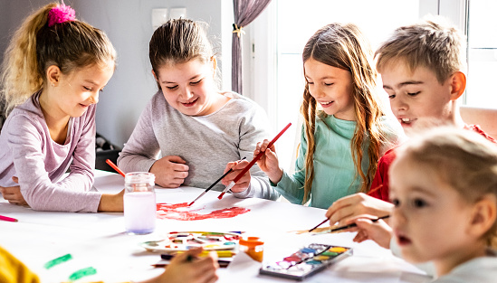 Group of kids sitting at the table and drawing and coloring with water colors