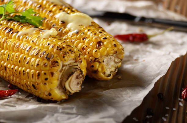 istock Kitchen table with grilled sweet corn cob under melting butter and greens on baking paper 1133161147
