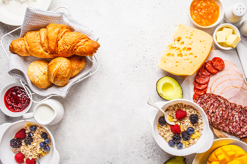 Continental breakfast table with croissants, jam, ham, butter, granola and fruit. Top view, food background.