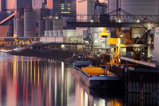 Coal-fired power plant on a canal at dusk with reflection in the water and barge with coal during unloading, High Dynamic Range image.