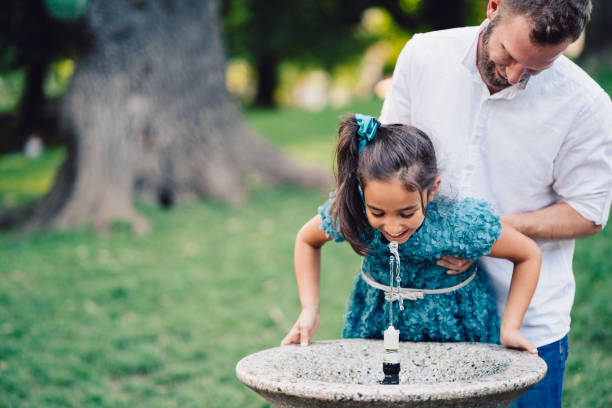 Father helping daughter to drink water in the park Young father and his daughter drinking water on hot summer day in the city park drinking fountain stock pictures, royalty-free photos & images