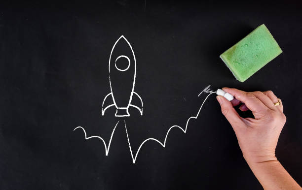 istock woman hand draws rocket launch on blackboard. 1133175186