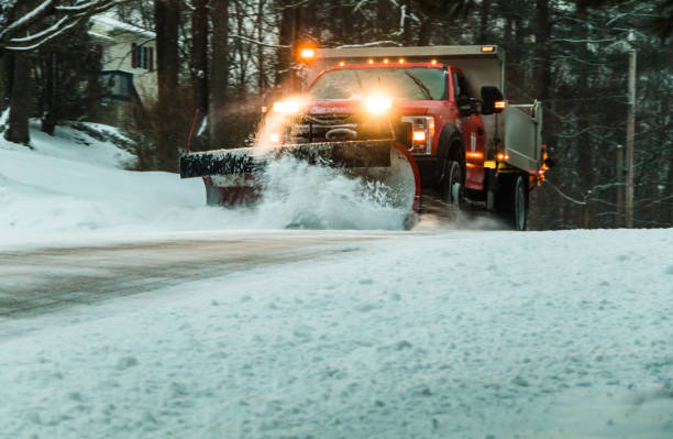 Snow plow at dusk maintains roads in a residential neighborhood during snow storm stock photo