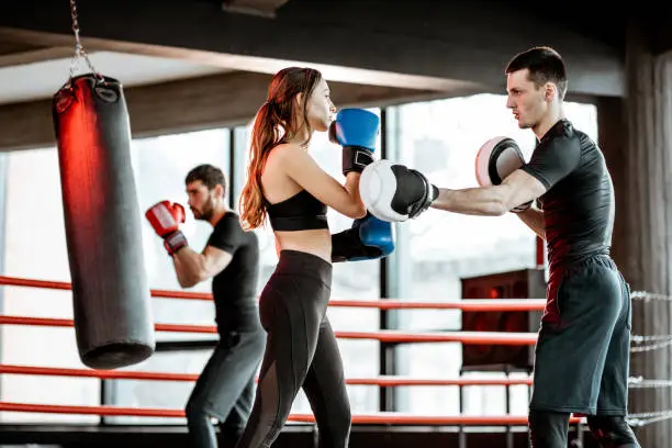 Young woman training to box with personal coach on the boxing ring at the gym