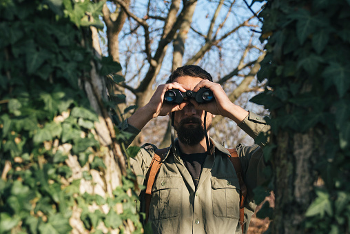 Man in the forest looks through binoculars