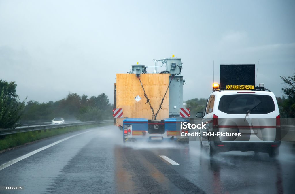 Austria, Graz, 09/14/2018: A safety escort vehicle following an oversized truck on the motorway Truck, Escort vehicle, Oversize, Motorway, Rain Heavy Stock Photo