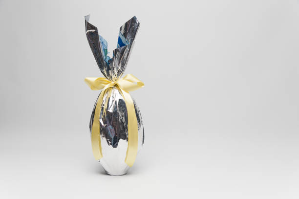 Homemade Easter egg in beautiful silver packaging with yellow ribbon. Isolated on white background. Horizontal image with space for text on the right.