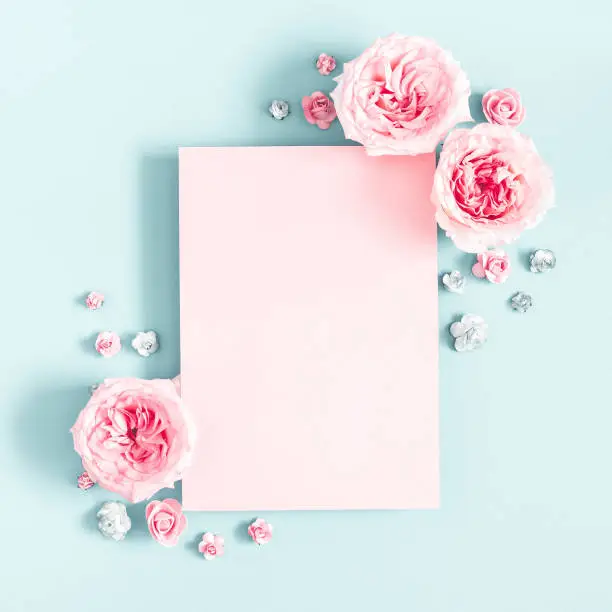 Photo of Flowers composition. Pink paper blank, rose flowers on pastel blue background. Valentines day, mothers day, womens day, spring concept. Flat lay, top view, copy space, square