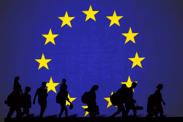 Silhouettes of refugees walking in front of the European Union flag with yellow stars on a blue background.