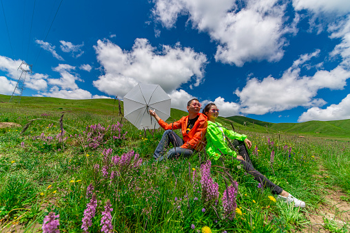 A couple sits on a plateau under blue sky and white clouds.