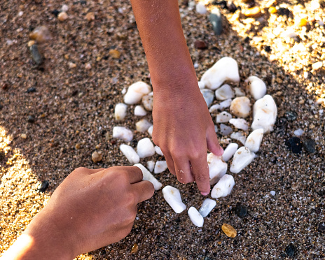 Kids hands close up making a heart of the white rocks