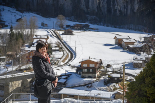 an asian female chinese tourist looking away at a small town in Switzerland