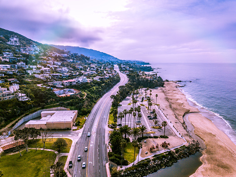 An aerial view of an early morning along the Laguna Beach coastline in Southern California. The famous Pacific Coast Highway is seen stretching along the coast with early morning vehicles traveling the highway.