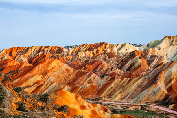 Rainbow Mountains in Zhangye Danxia Landform Geological Park. Incredible Colorful View of Rainbow Mountains Geological Park. Stripy Zhangye Danxia Landform Geological Park in Gansu Province, China. Sharp Peaks and Road in a Valley on a Sunny Day. danxia landform stock pictures, royalty-free photos & images
