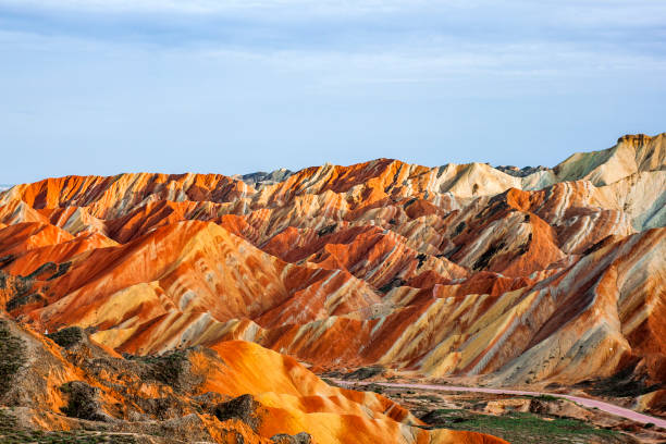 Rainbow Mountains in Zhangye Danxia Landform Geological Park. Incredible Colorful View of Rainbow Mountains Geological Park. Stripy Zhangye Danxia Landform Geological Park in Gansu Province, China. Sharp Peaks and Road in a Valley on a Sunny Day. zhangye danxia geopark china stock pictures, royalty-free photos & images
