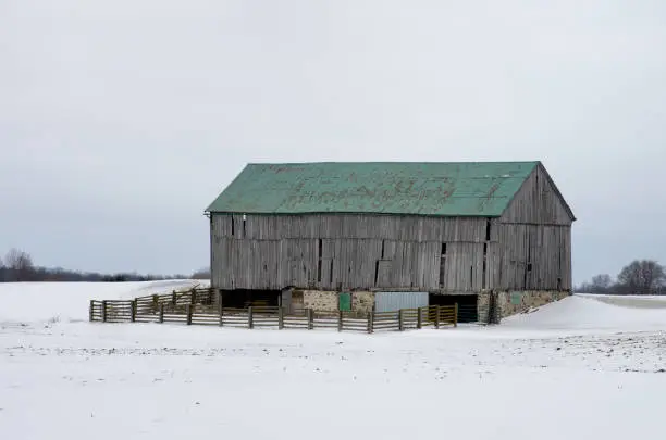 A plain old wood barn in a rural snow covered winter setting.
