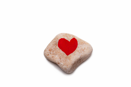A studio shot of a pebble with a red heart on it on a white background