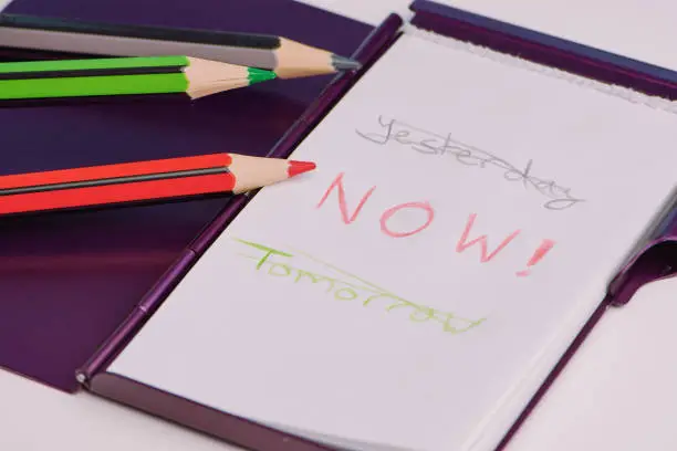 handwritten text with the words: yesterday, now and tomorrow on a white notepad as a concept to live in the moment