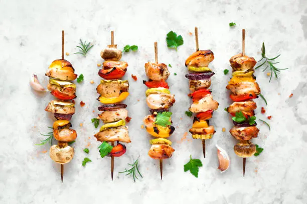 Grilled vegetable and chicken skewers with  bell peppers, zucchini, onion and mushrooms on white marble background, top view. Meat and vegetables kebabs on skewers.