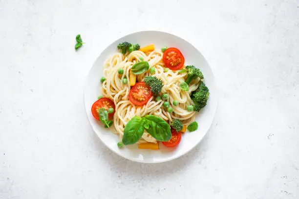 Pasta Primavera. Spaghetti pasta with vegetables and basil, top view, copy space. Vegetarian seasonal pasta primavera recipe.