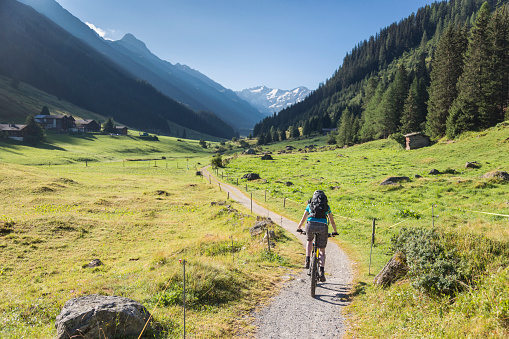 A female mountain biker is riding on a footpath in the morning into scenic Dischma Valley nearby Davos which is a large alpine city in the canton of Graubünden. The region is famous for lots of outdoor sports activities in summer as well as in wintertime.\nCanon EOS 5D Mark IV, 1/500, f/4, 32 mm.