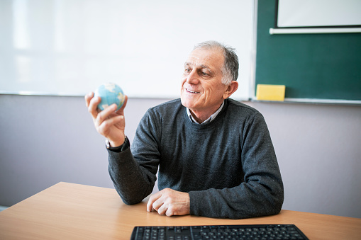 Old professor holding in hand and looking at small globe