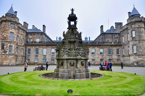 Edinburgh, Scotland, UK - May 27, 2018: Built in the late 17th century, Palace of Holyroodhouse is Her Majesty The Queen’s official residence in Scotland. Tourists gather around the forecourt fountain before entering the palace grounds.