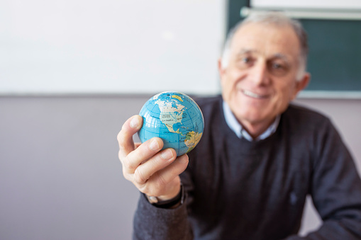 Senior teacher holding in hand and looking at small globe