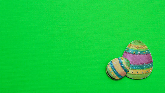 Two decorated Easter eggs laying flat on a green background with writing space